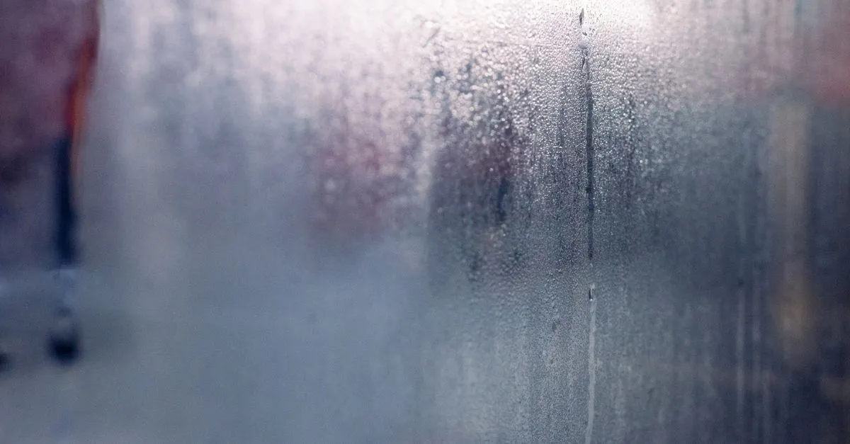 Moisture droplets on a foggy window create a mysterious and serene atmosphere.